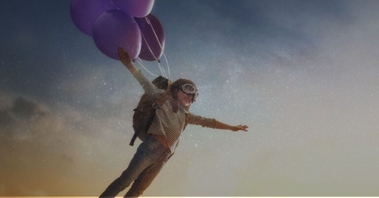 child with goggles being lifted in the air by balloons